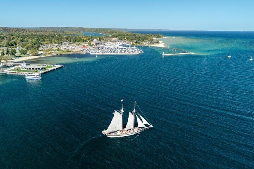 A sailboat on a calm sea with a marina and buildings in the background. 3
