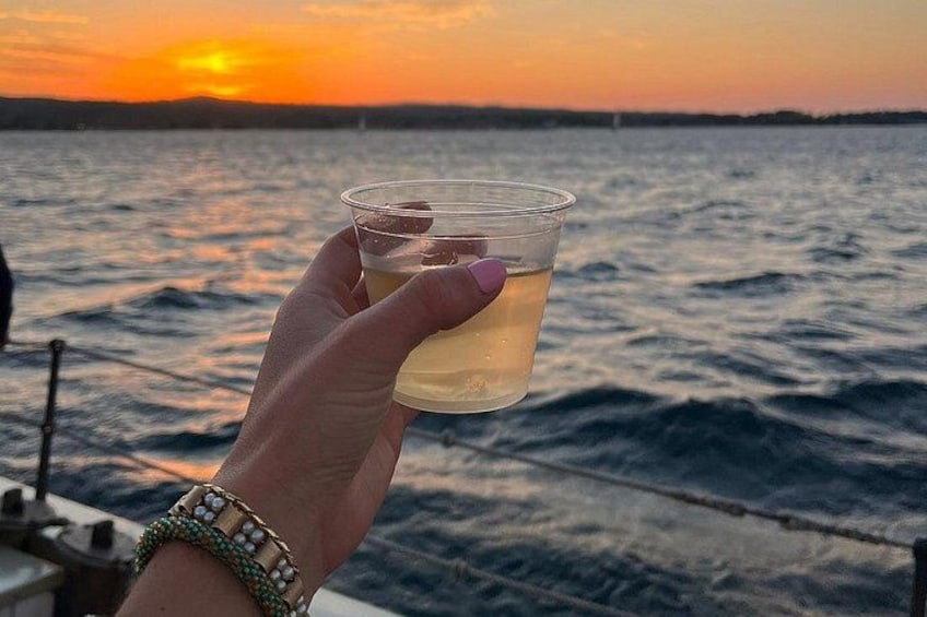 A hand holding a glass of liquid against a sunset over water. 3