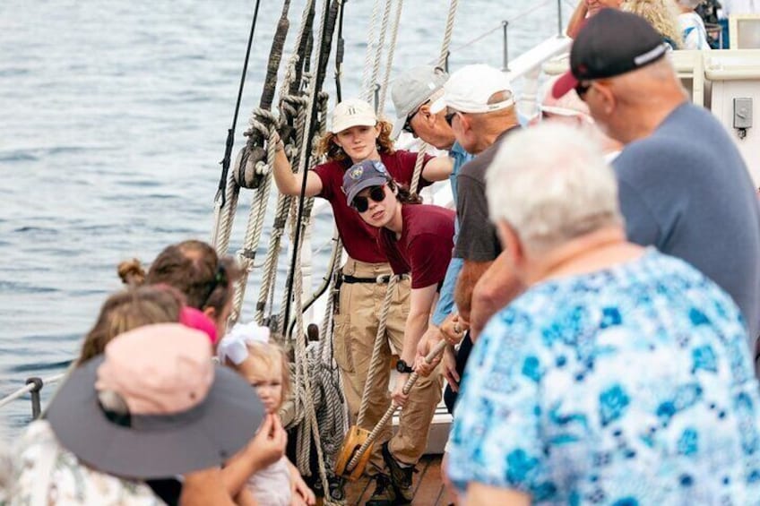 A group of people on a sailboat, with one person in a life jacket and another in a maroon shirt. 2