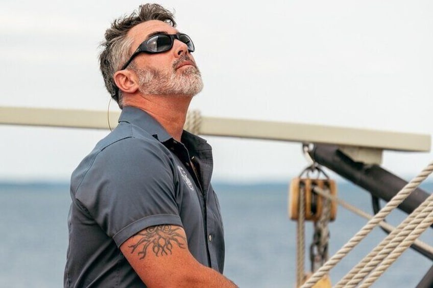 A man on a boat with a tattoo on his arm, ropes, and the sea in the background. 5