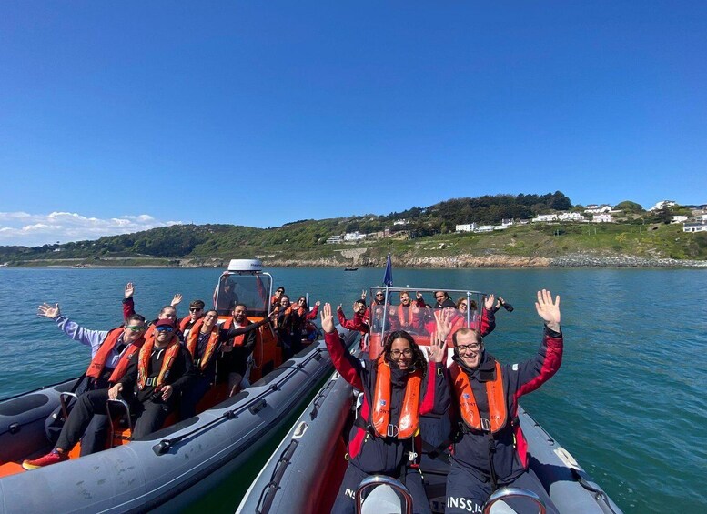 A group of people on a boat wearing life jackets, with a clear sky and a hilly landscape in the background. 1