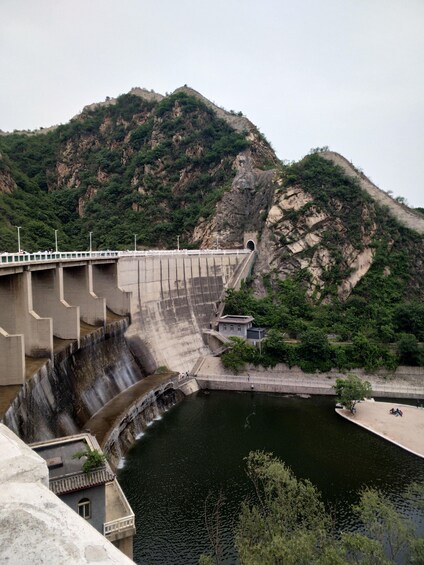 A dam with a water spillway, a bridge, and a mountainous backdrop. 3