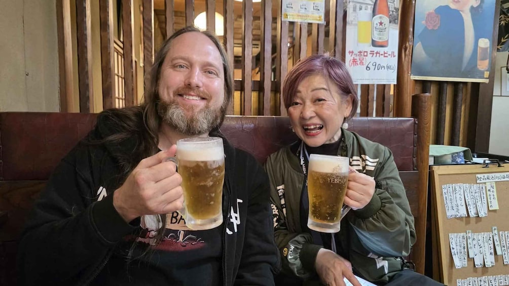 Two people sitting on a bench, holding glasses of beer. 2