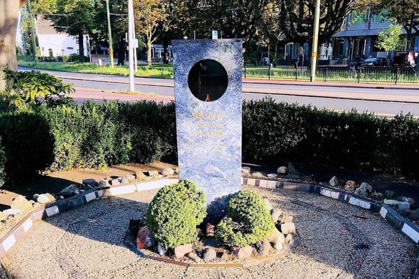 Ein Steinsockel mit Inschriften, umgeben von einem Kiesweg und geschnittenen Hecken. 2