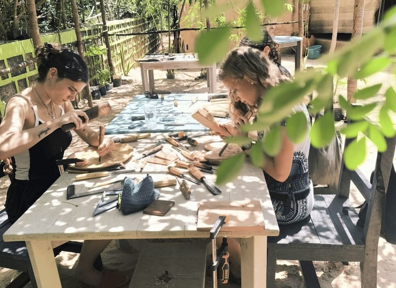 Two individuals engaged in woodworking, surrounded by tools and materials on an outdoor table. 3