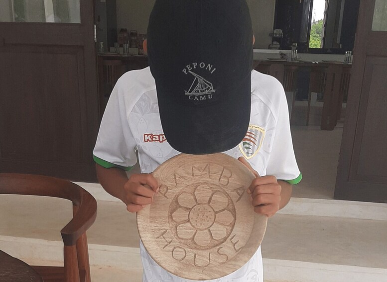 A child holding a wooden plaque with a flower design and the words 'RAMPAGE MOISE' engraved on it. 2