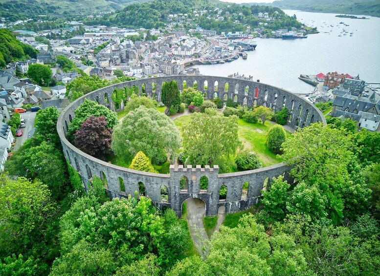 A circular stone structure surrounded by lush greenery, overlooking a town and a harbor. 1