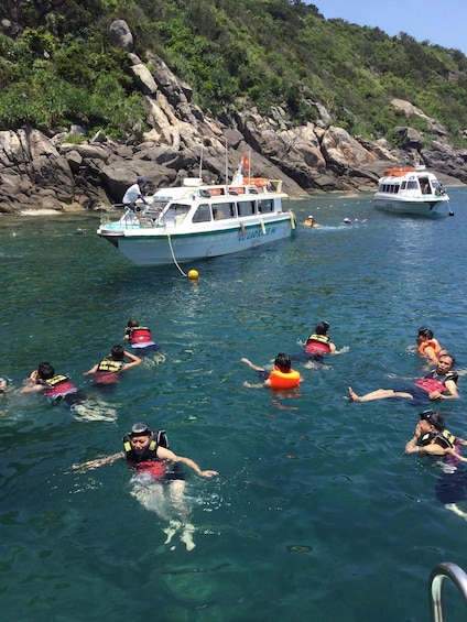 People snorkeling in clear water with boats in the background. 3