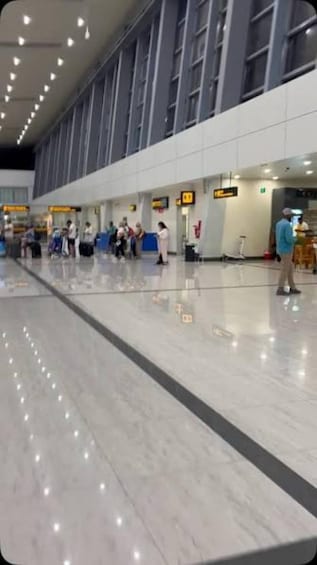 A spacious indoor area with a marble floor, large windows, and people standing in line. 1