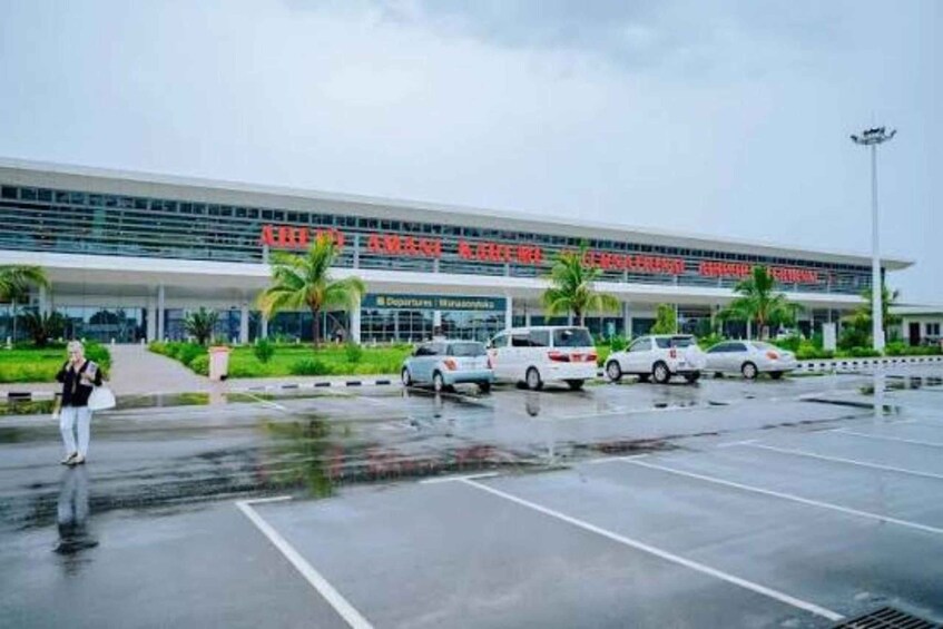 A modern building with a sign that reads 'Airport Terminal.' There are cars parked in front, and palm trees are visible. 2