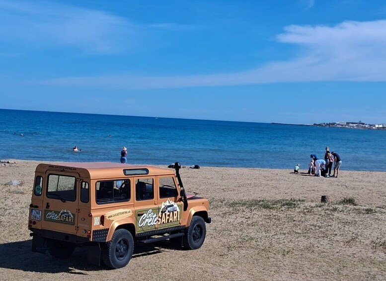 A beige off-road vehicle with 'Crete Safari' branding parked on a sandy beach. 2