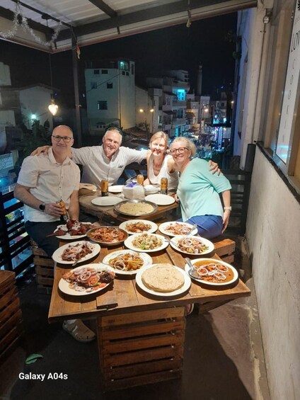 Un grupo de personas cenando al aire libre de noche, con diferentes platos en una mesa de madera. 1