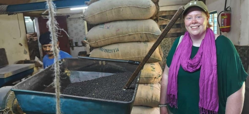 A person standing next to a large blue container filled with black pellets, with sacks labeled in the background. 4