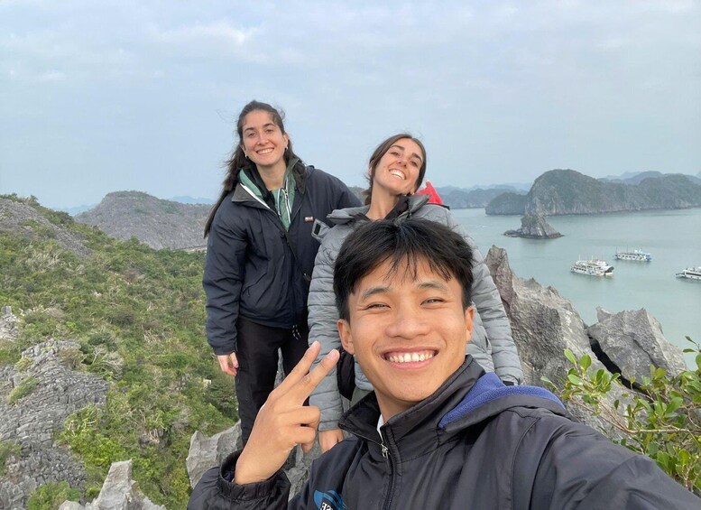 Three people on a rocky outcrop with a view of boats on a calm sea and distant mountains. 4