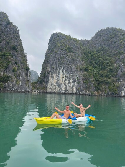 Two people in a yellow and blue kayak on calm water with rocky cliffs in the background. 3
