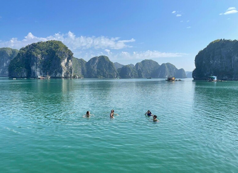 A calm sea with people swimming and boats anchored near limestone cliffs. 5