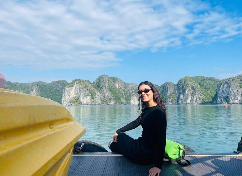 A person sitting on a dock with a yellow boat in the foreground and a mountainous landscape in the background. 1