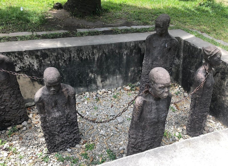 Three stone statues of chained figures in a garden setting. 2