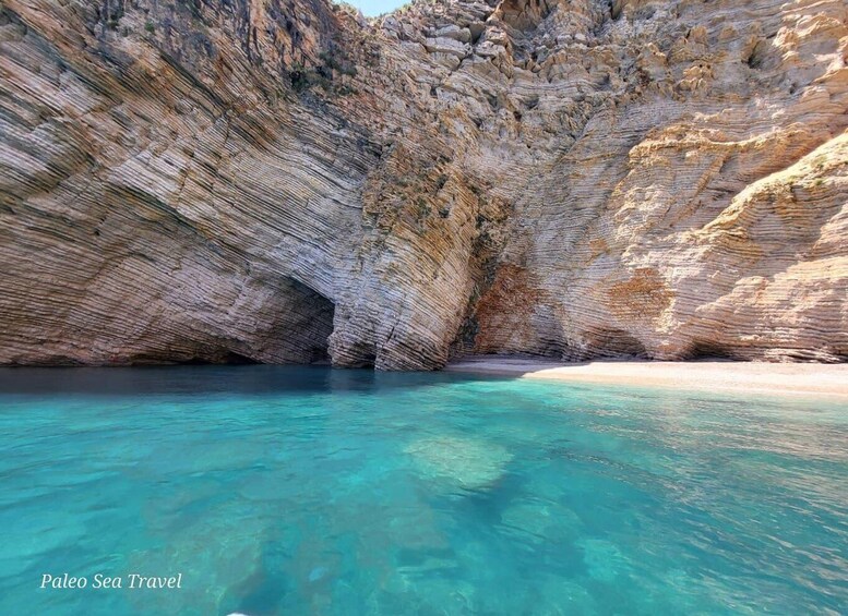 A clear blue sea with a rocky cliff and a sandy beach. 1