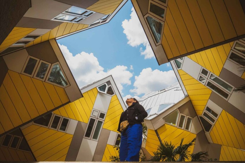 A person standing in front of a yellow and white geometric building with multiple windows. 1