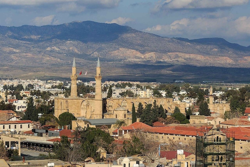 A cityscape with a prominent mosque featuring two minarets, surrounded by residential buildings and mountains in the background. 3
