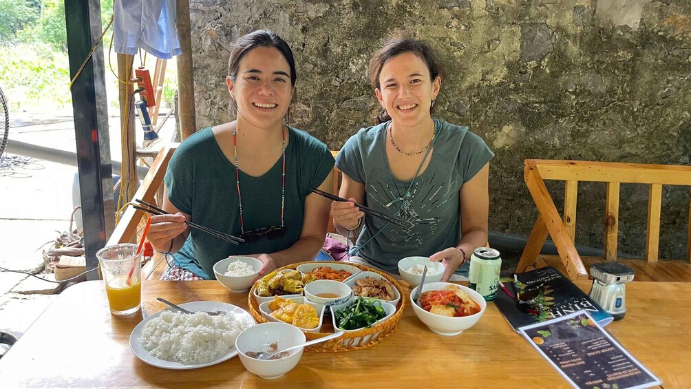 Two people sitting at a table with a variety of dishes, including rice, vegetables, and a drink. 3