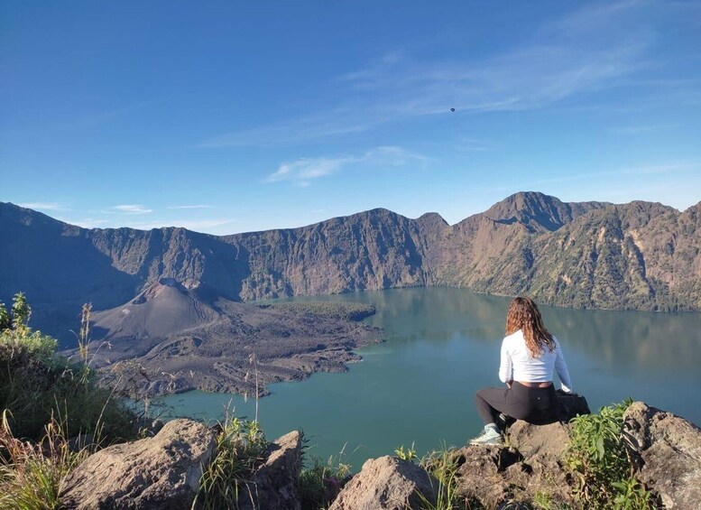 A person sitting on a rock overlooking a lake surrounded by mountains. 1