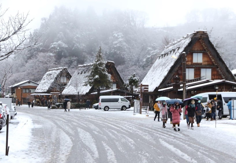 A snowy village with traditional houses, a road, and people walking. 2