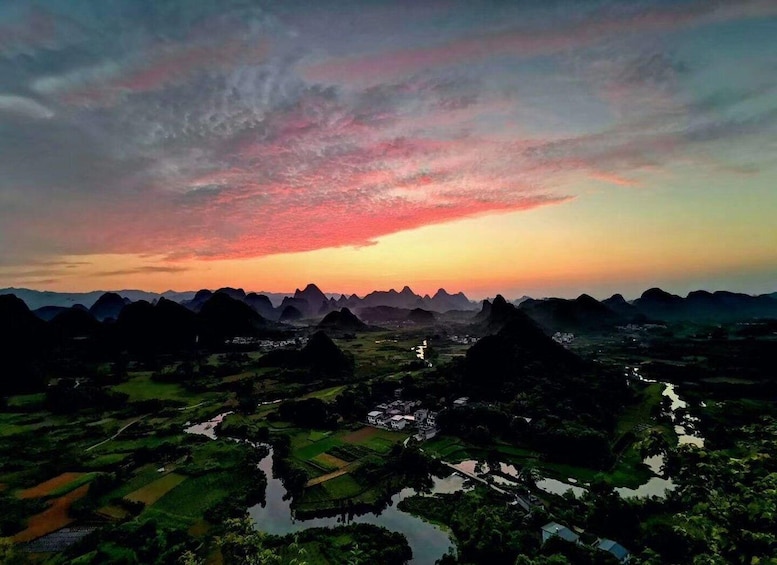 A landscape with a river, fields, and mountains during sunset. 4