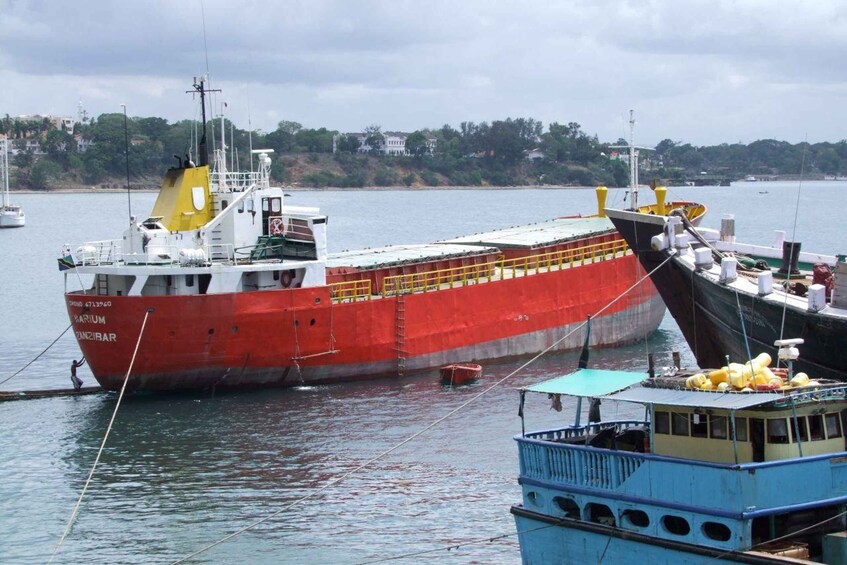 A large red cargo ship docked at a port with a smaller blue boat nearby. 1