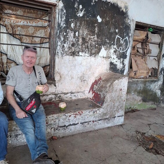 A man sitting on a bench in a weathered building with peeling paint and a worn-out door. 5