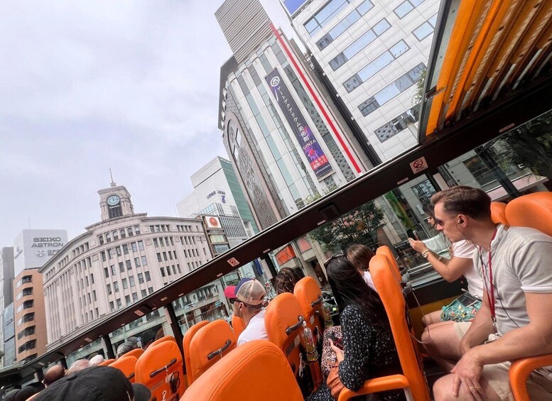 A bus with passengers, a clock tower, and modern buildings in the background. 2