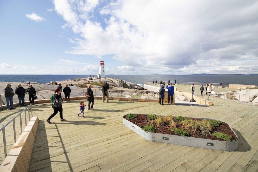 A coastal promenade with a lighthouse, rocky terrain, and people walking. 2