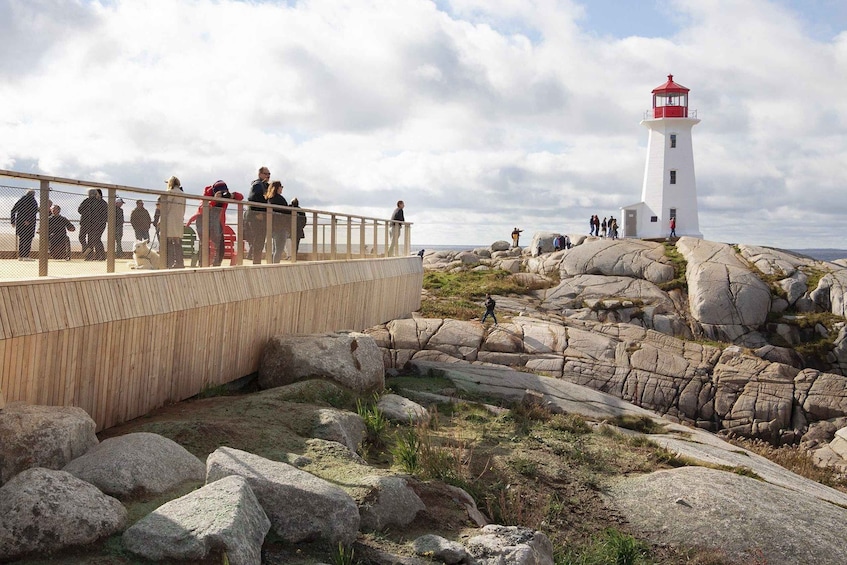 A lighthouse on a rocky outcrop with people walking on a wooden bridge. 4