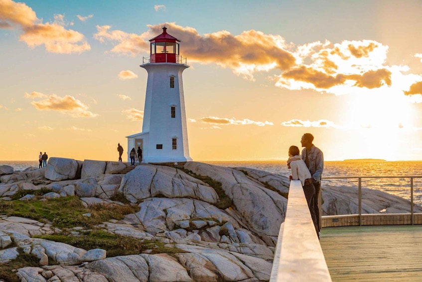 A lighthouse on a rocky shore with people standing on a pier. 1