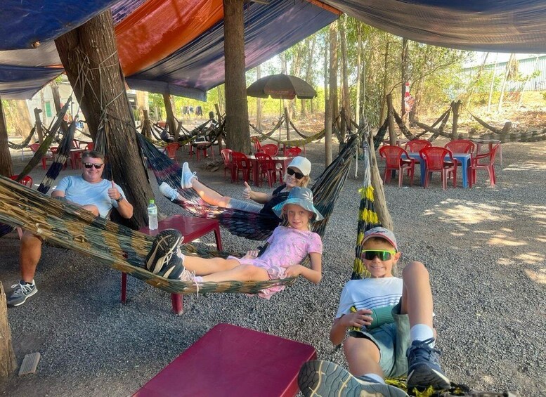People relaxing in hammocks under a shaded area with red plastic chairs in the background. 4