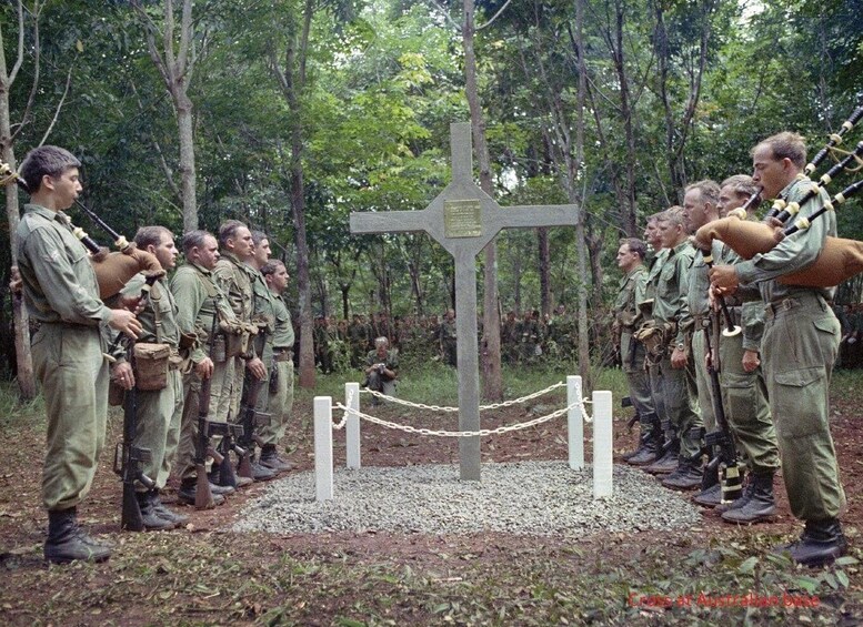 Soldiers in uniform standing in a forest with a cross monument in the center. 2