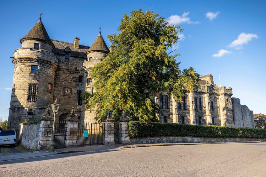 A historic stone castle with multiple towers and a large tree in front. 4
