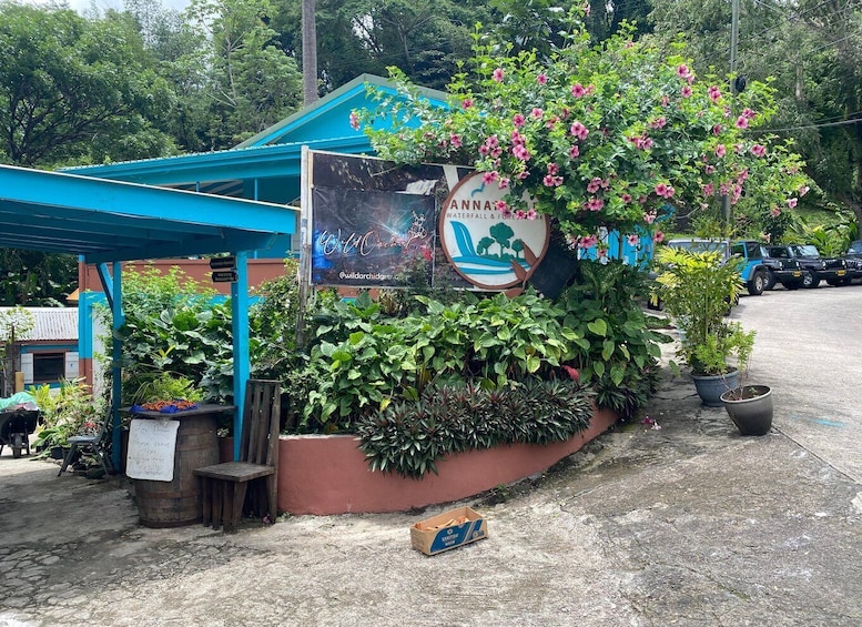 A roadside sign for a waterfall and forest park, surrounded by lush greenery and parked vehicles. 5