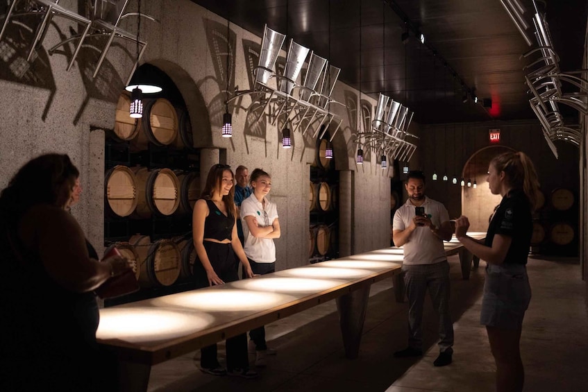 A group of people standing in a dimly lit room with wine barrels and hanging lights. 3