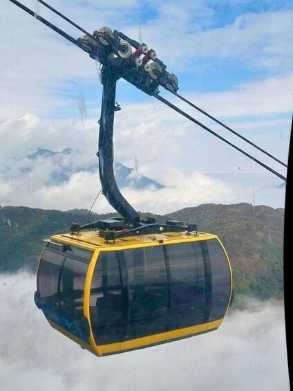 A cable car suspended above clouds with a mountainous landscape below. 1