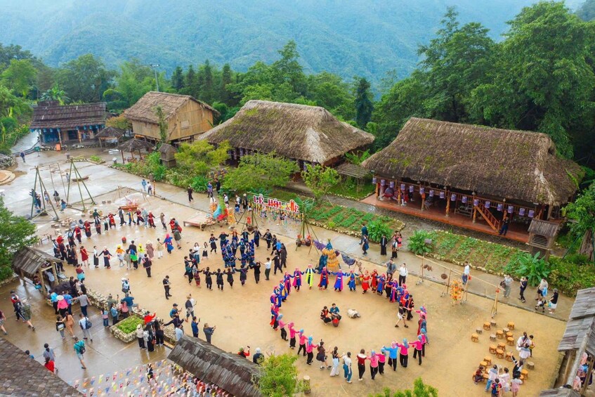 A village with thatched-roof houses, a central gathering of people in colorful attire, and a mountainous backdrop. 4