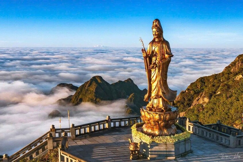 A golden statue on a mountain peak with a sea of clouds below. 5