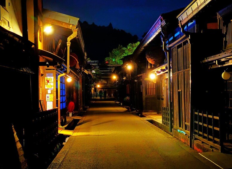 A narrow street at night with illuminated buildings and a clear sky. 1
