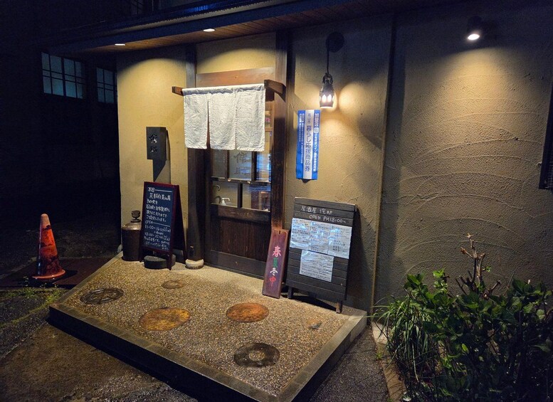 A restaurant entrance with a signboard, a towel hanging on the door, and a small garden area with plants. 4