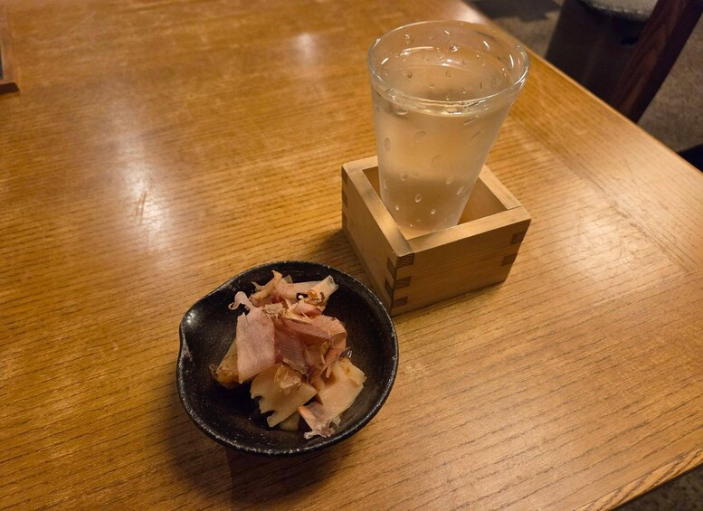A wooden table with a glass of iced beverage and a small bowl of pickled vegetables. 5