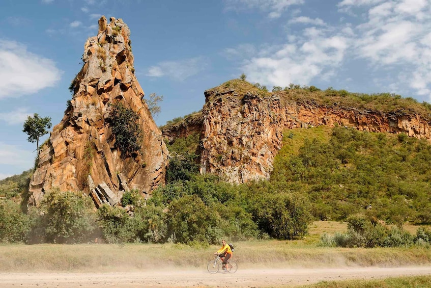 A person riding a bicycle on a dirt path with a large rock formation in the background. 1