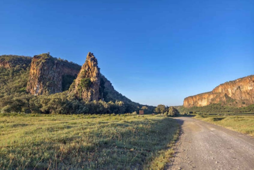 A dirt road leading through a grassy field with a prominent rocky outcrop on the left and a large hill on the right. 5