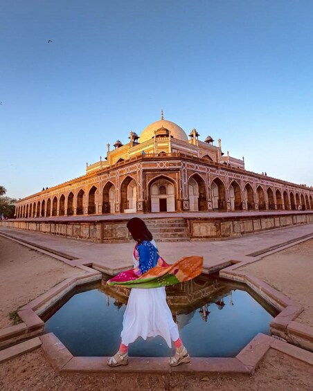 A person standing in front of a large, ornate building with a dome and arches, near a reflective water feature. 3