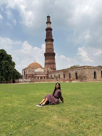 A person sitting on grass in front of a large historical building with a prominent tower. 4